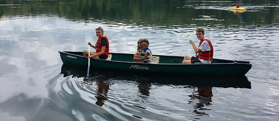 Four individuals riding a canoe in a lake together during YMCA-run camp